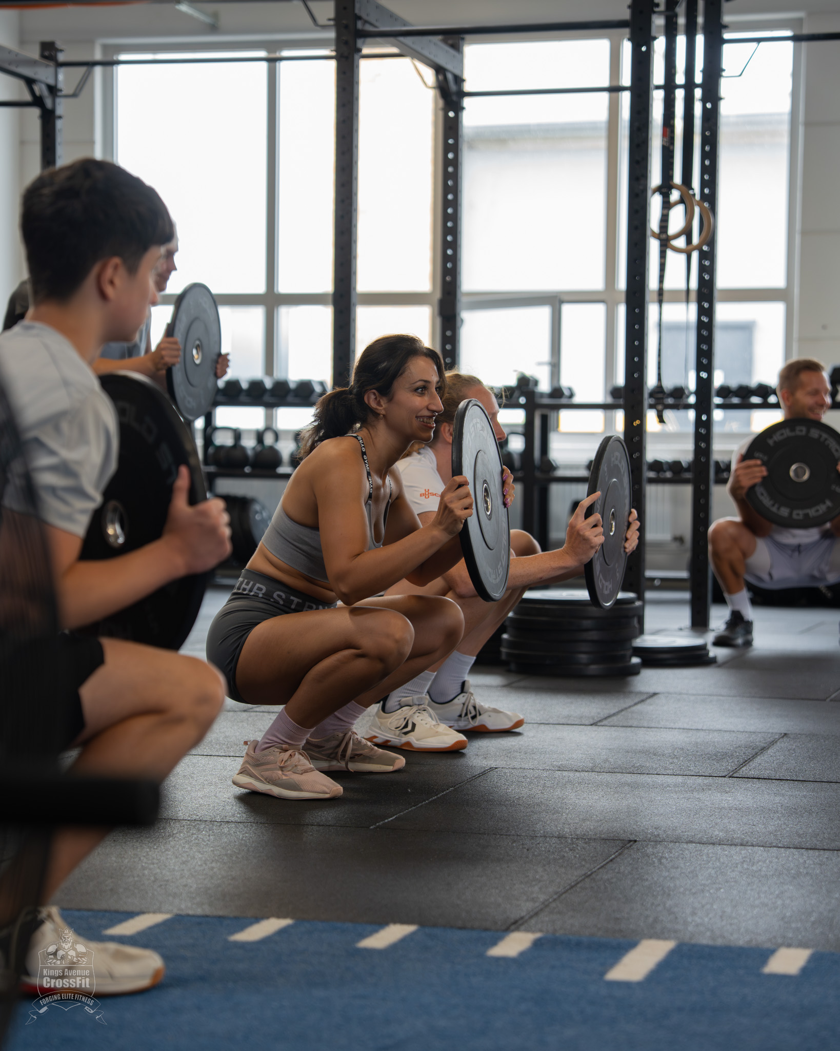 Teilnehmende üben Kniebeugen mit Gewichtsscheiben beim Tag der offenen Tür von Kings Avenue CrossFit