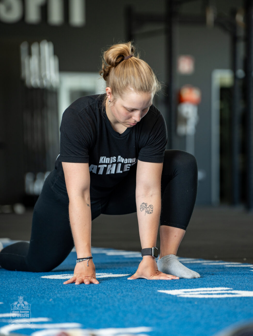 Athletin dehnt die Hüfte im tiefen Ausfallschritt, beide Hände auf der blauen Trainingsfläche